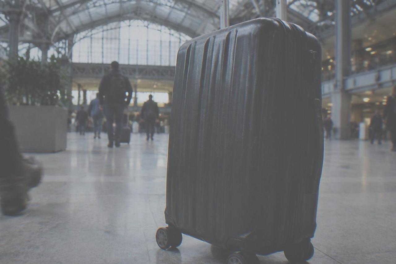 Wide view of the Moynihan Train Hall concourse with travellers pulling wheeled suitcases across a bright stone floor