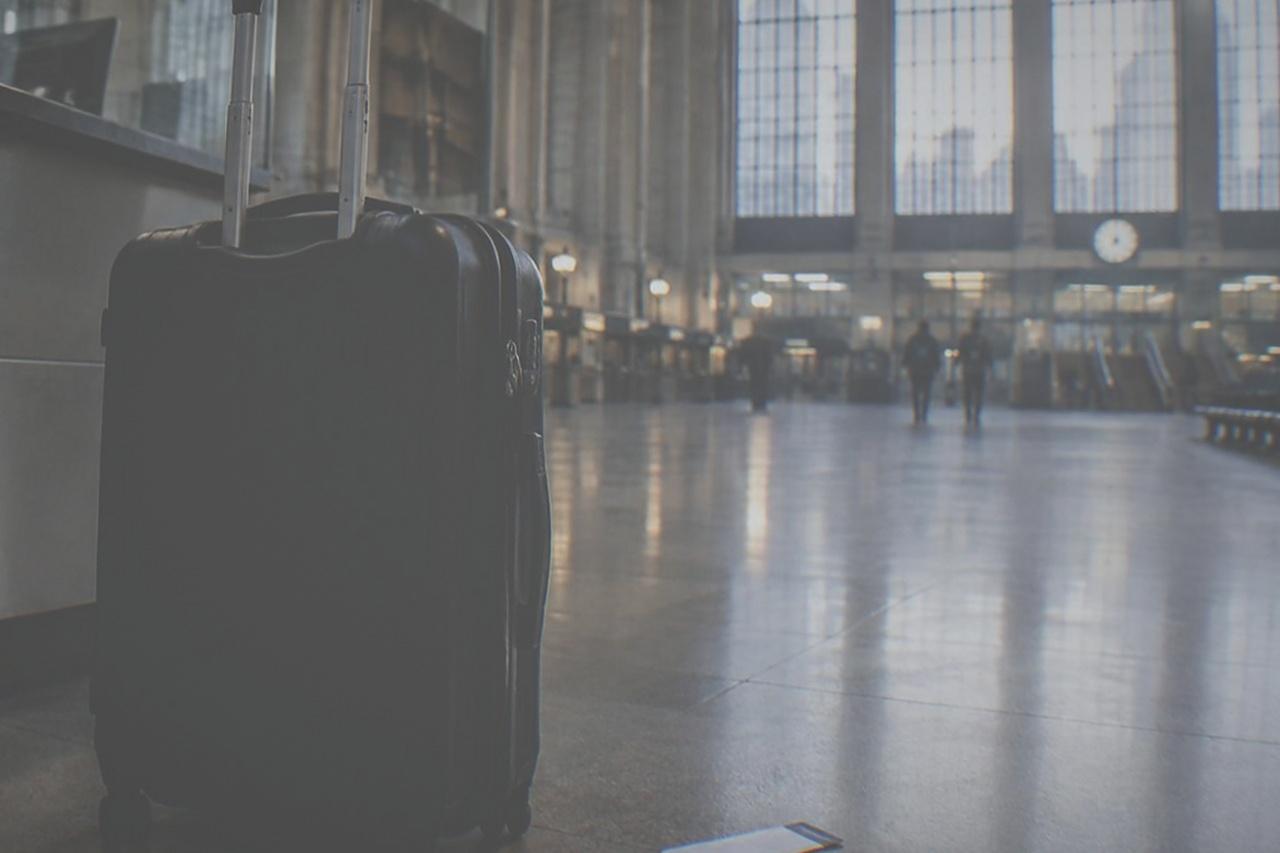 A closed airline check-in counter in an empty airport terminal with a single suitcase waiting beside it