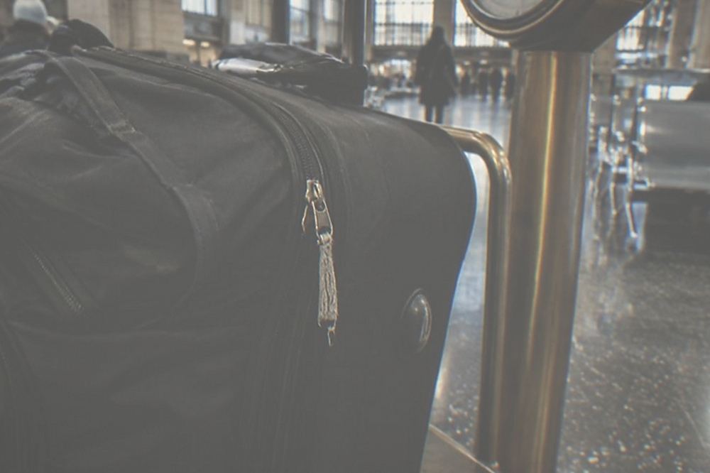 A large wheeled suitcase standing beside a luggage scale in a station waiting area