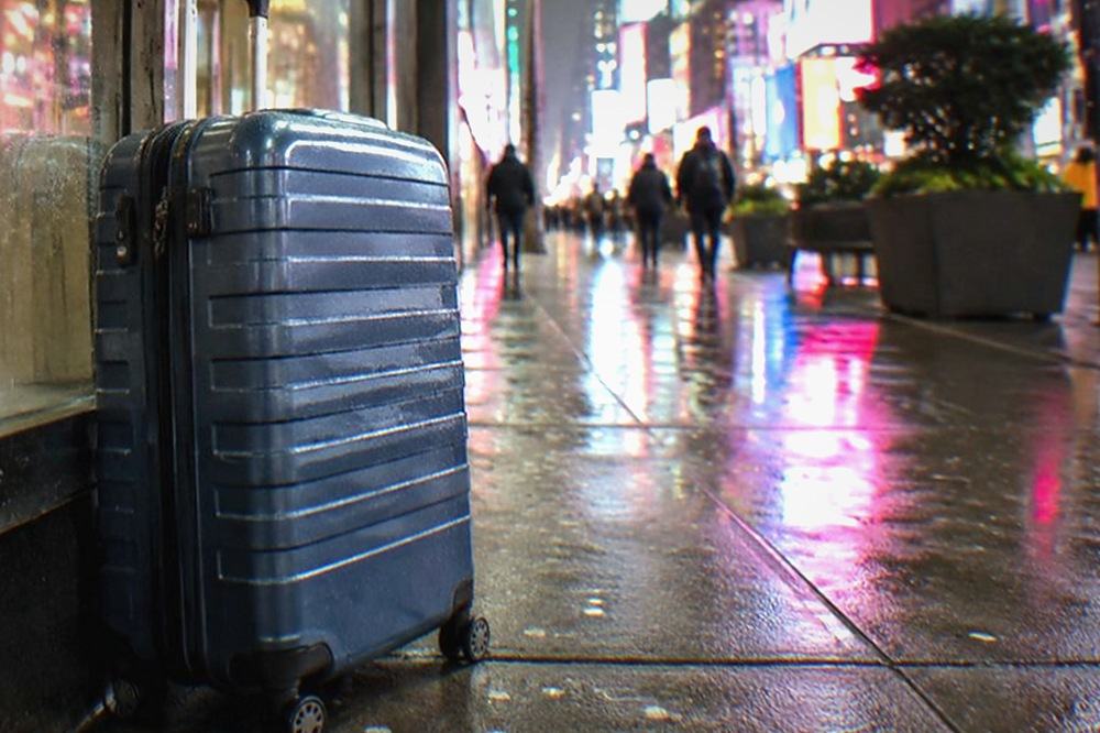 Suitcase parked on a sidewalk beside a shop doorway with a storage point sign in the window