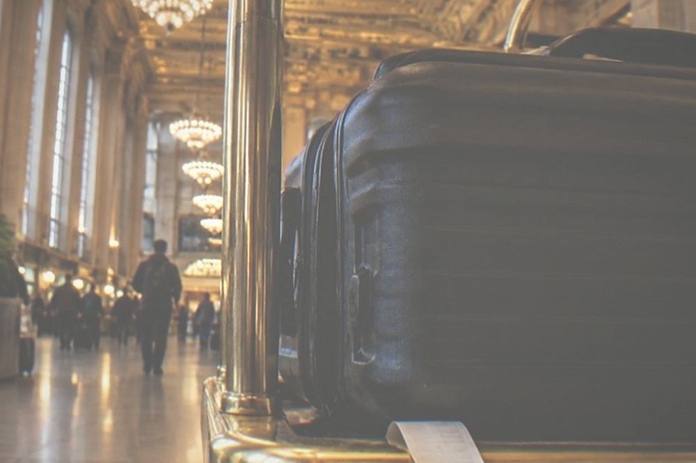 Rolling suitcase parked beside a hotel luggage cart under a lobby chandelier