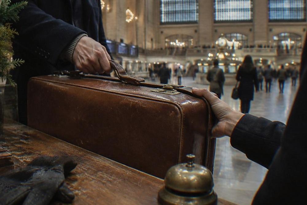 A traveller handing a suitcase across a shop counter in a Manhattan store
