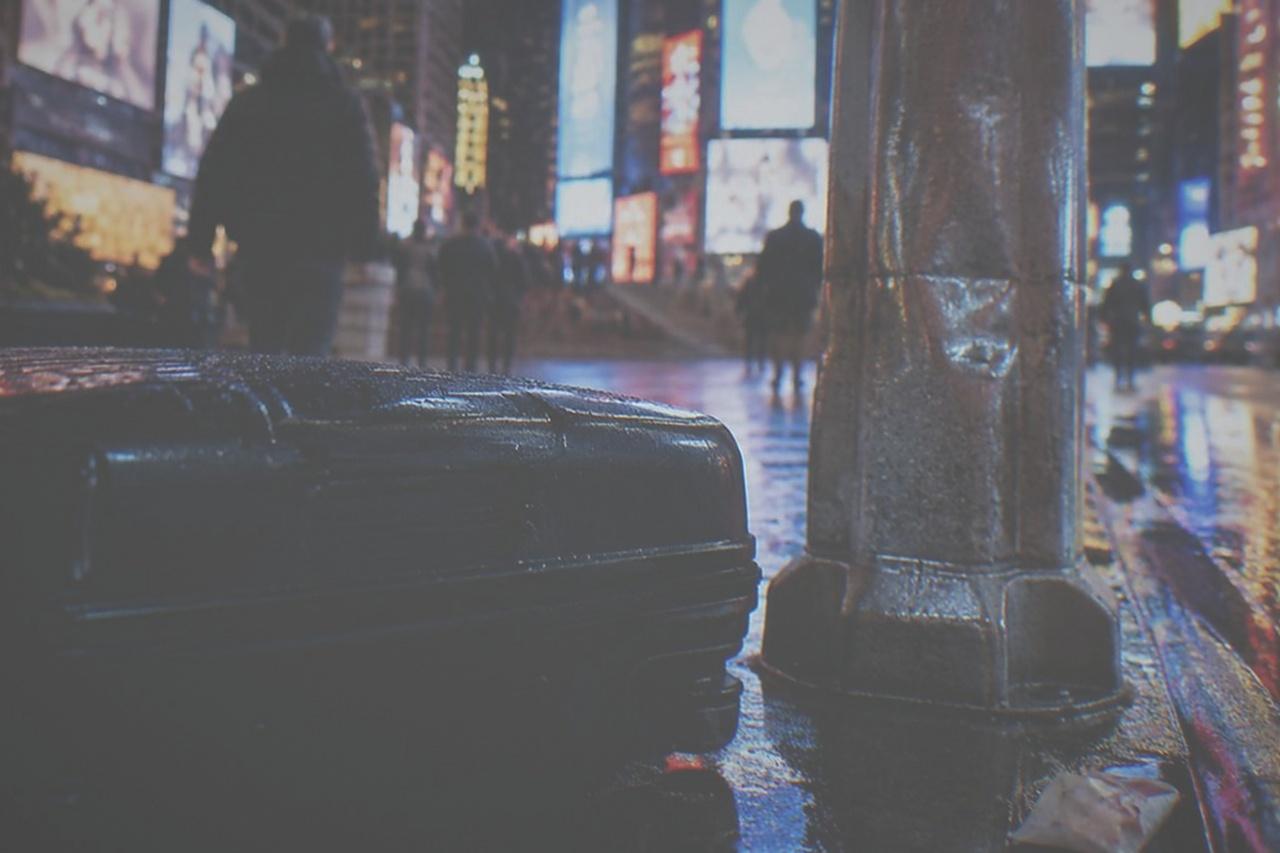 An empty Manhattan sidewalk with a closed suitcase standing beside a parking sign
