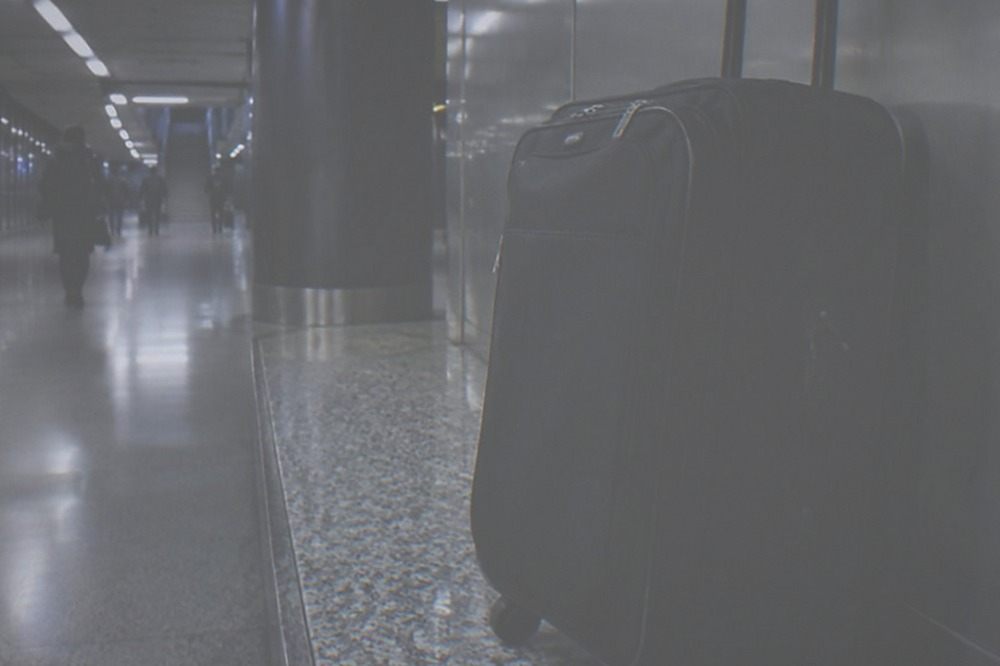 Airport terminal corridor at night with polished floors, lit signage and an unattended luggage trolley against a wall