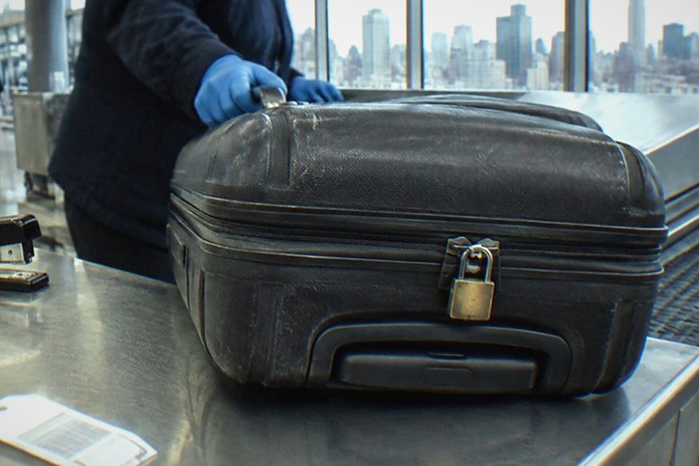 A staffed airport baggage storage counter with a suitcase being handed across the desk