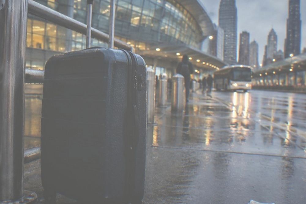 A bus stop outside an airport terminal with a suitcase standing beside the shelter