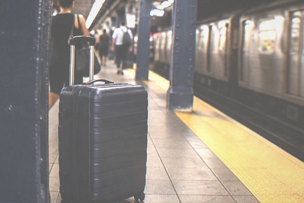 A subway platform with a large wheeled suitcase waiting behind the yellow safety line