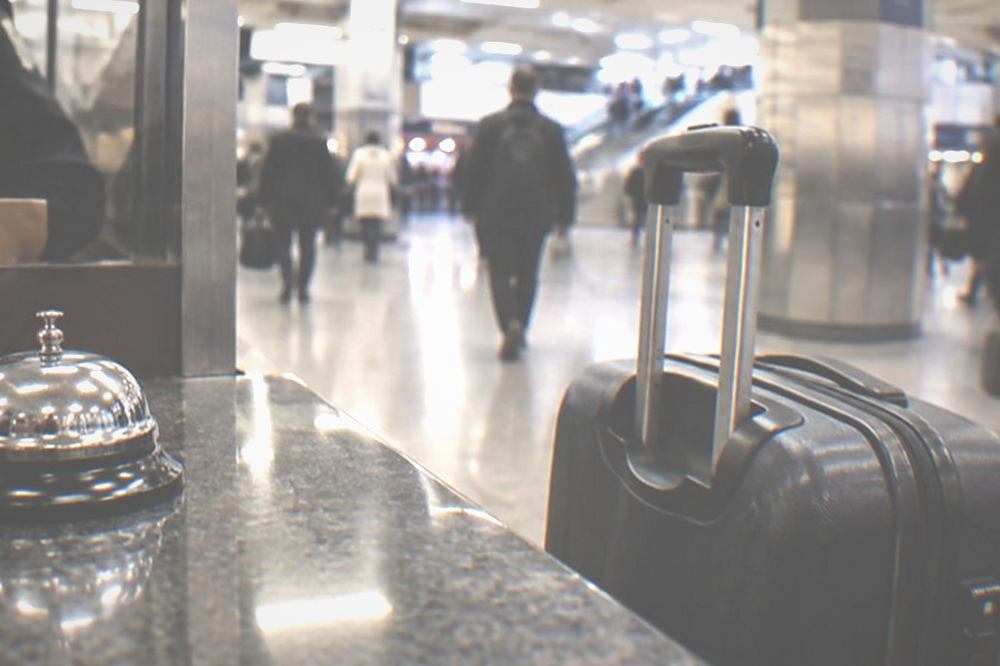 A hotel front desk counter in New York with a bell and a suitcase standing beside it.