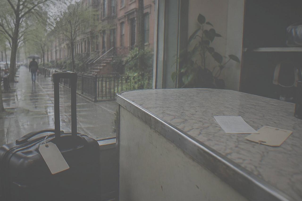 A suitcase resting beside the counter of a small New York shop, with a numbered tag and receipt on the countertop.