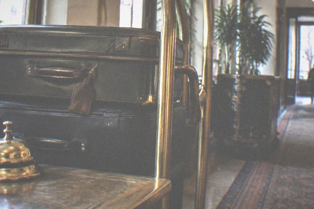 A hotel bell desk with a luggage rack holding two suitcases, a brass bell on the counter, empty lobby corridor beyond