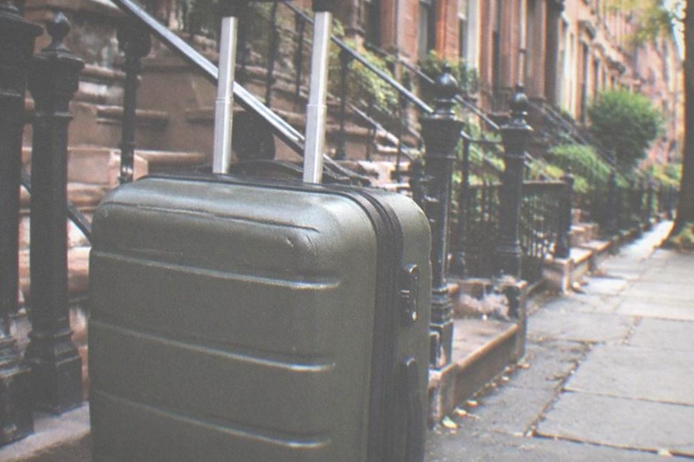 Brownstone street corner in Brooklyn with a shopfront and a person pulling a rolling suitcase