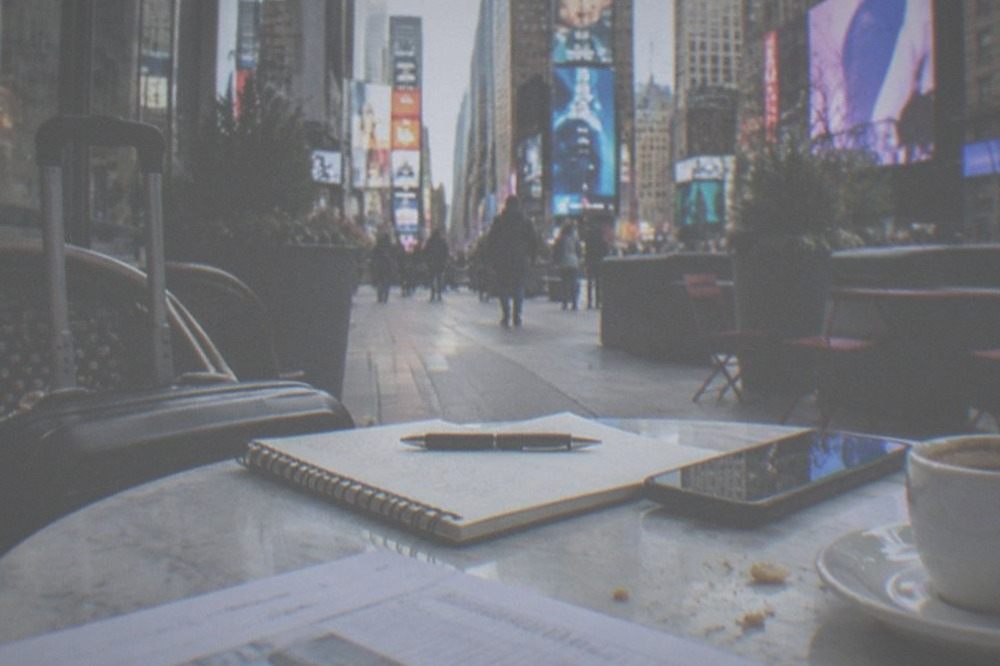 Notebook and phone on a cafe table beside a suitcase with a printed confirmation