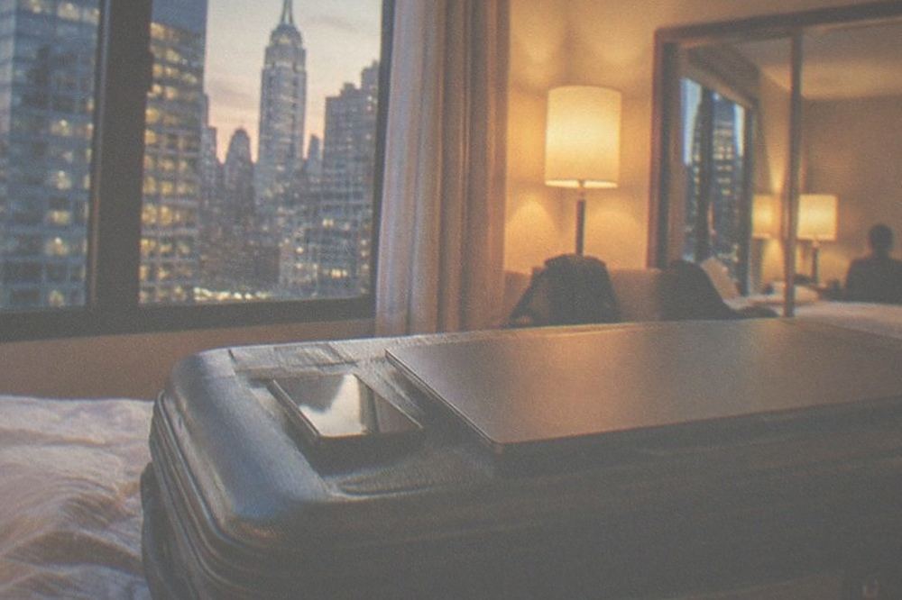 A laptop and phone placed on a suitcase lid in a hotel room