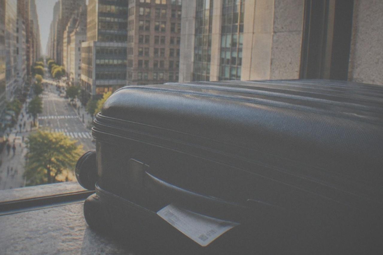 An empty Manhattan sidewalk in late afternoon light with a closed suitcase standing beside a parking sign